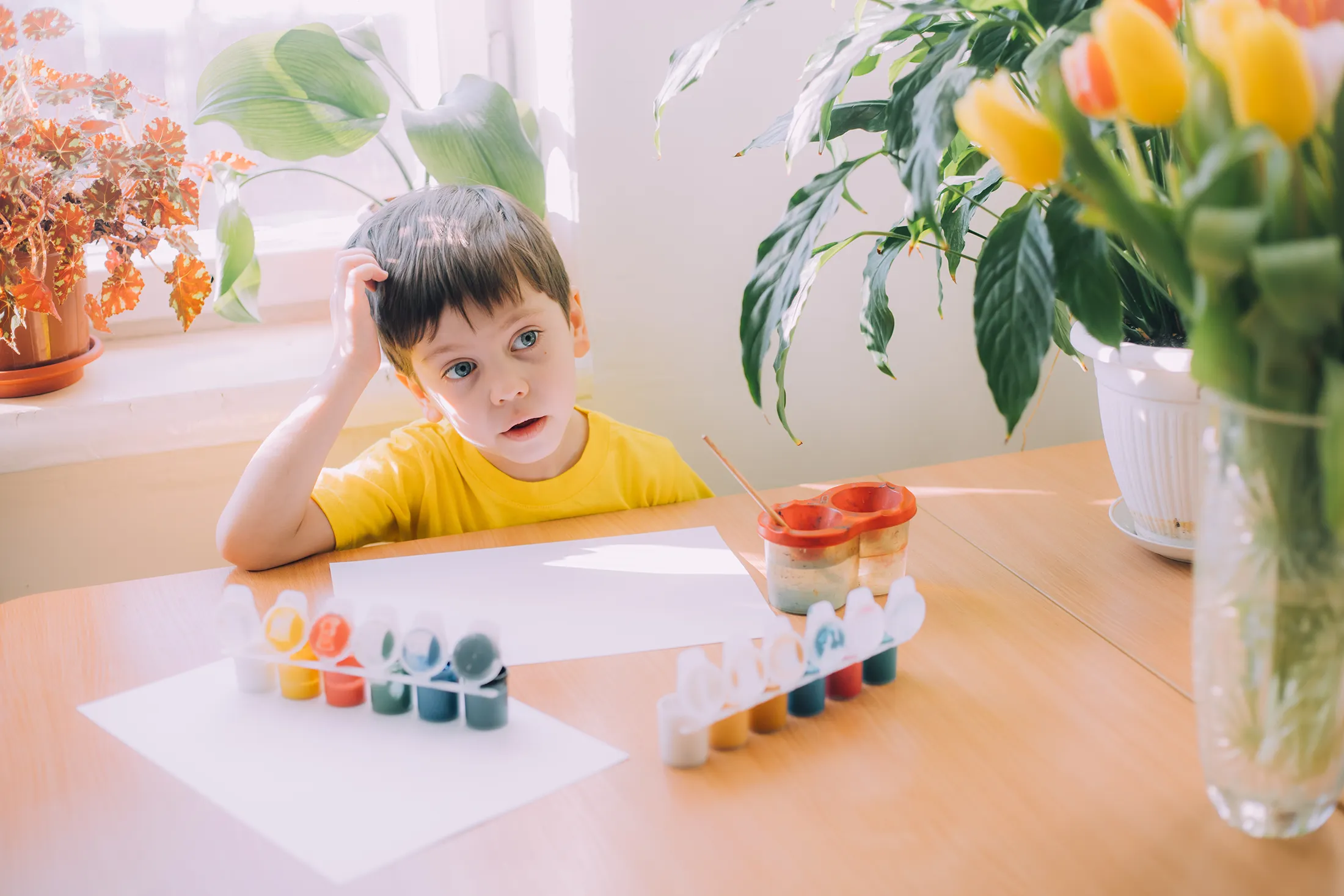 a-boy-paints-a-lifestyle-2024-10-18-06-02-32-utc Child sitting at a table looking tired while painting, illustrating signs baby is sick and the importance of visiting a pediatrician in McKinney to check for developmental or health concerns.