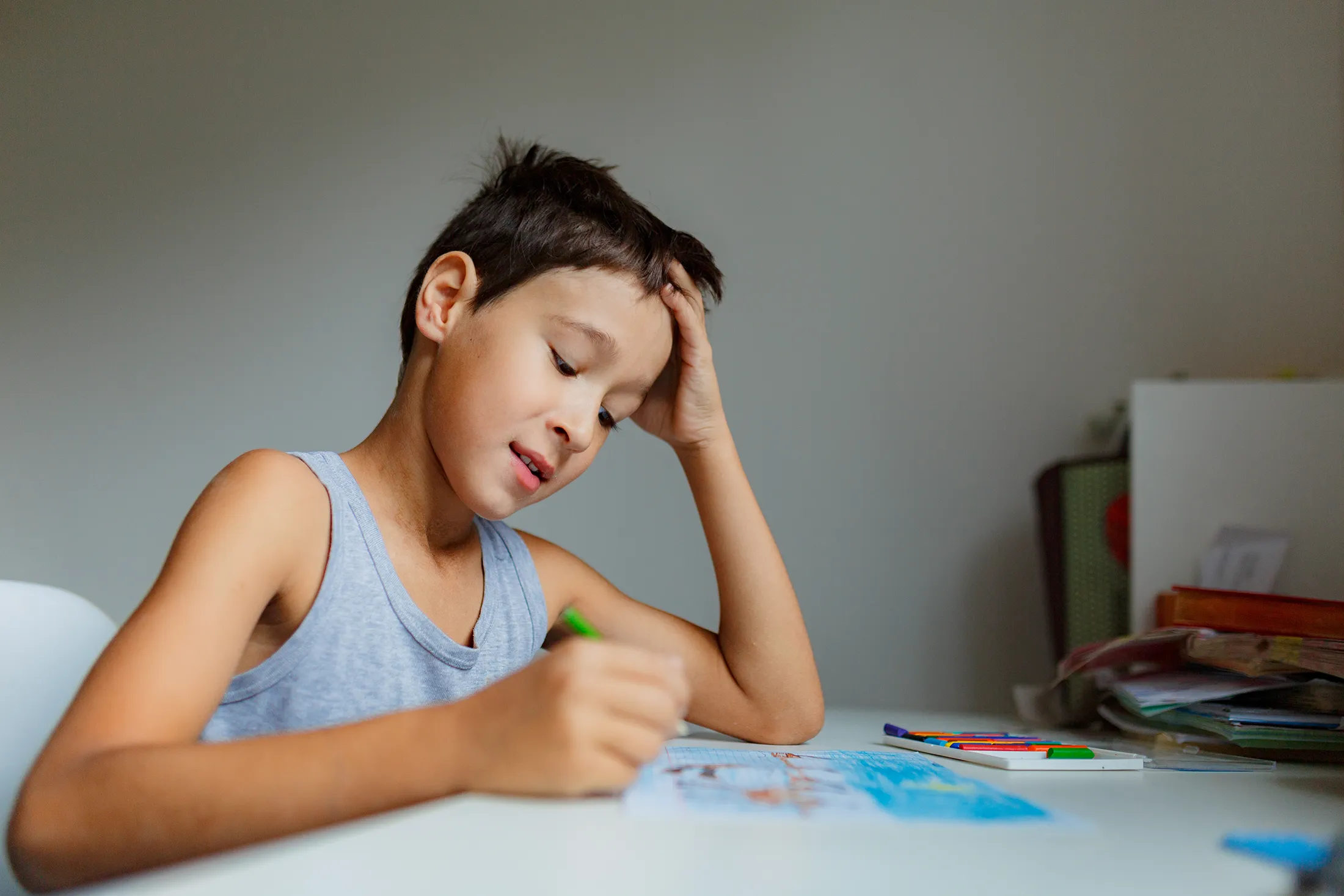 dark-haired-boy-draws-a-picture-with-pencils-whil-2024-10-13-21-23-03-utc Young boy concentrating while drawing with colored pencils at a desk.