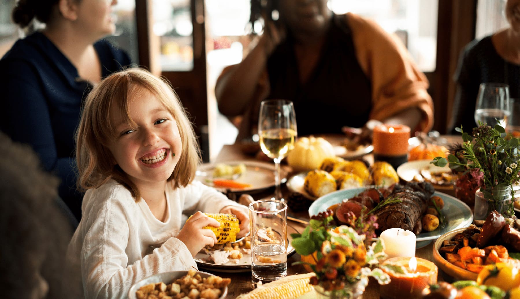 a little girl and her family sitting at a table full of food for Thanksgiving laughing and being merry