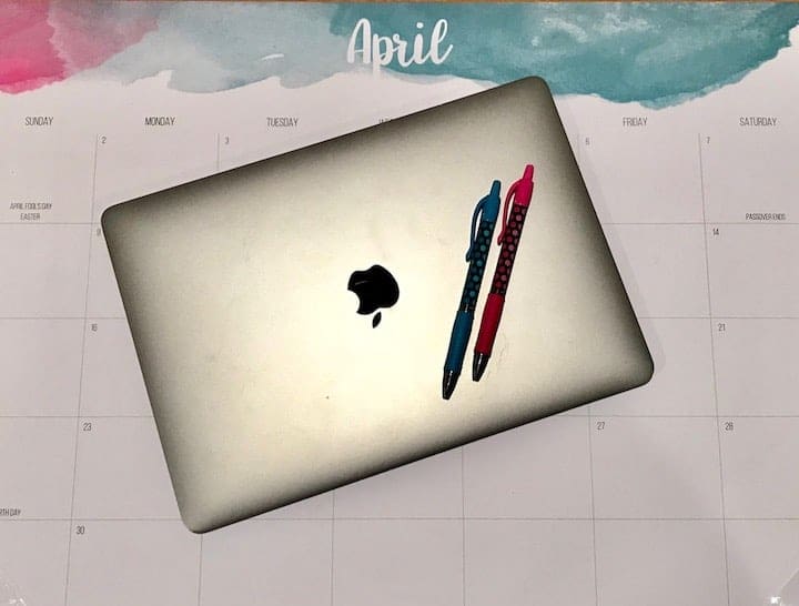 April calendar with a apple laptop and two pens on top of it