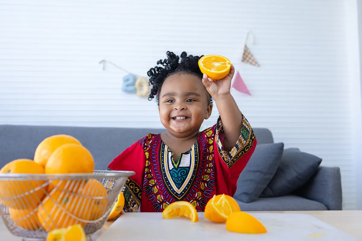 African baby holding an orange slice Cute African baby girl showing the halved orange fruit in hand.