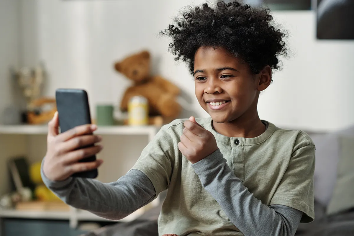 Schoolboy taking a selfie with a smartphone Happy schoolboy holding smartphone in front of himself and taking selfie, (social media boundaries)