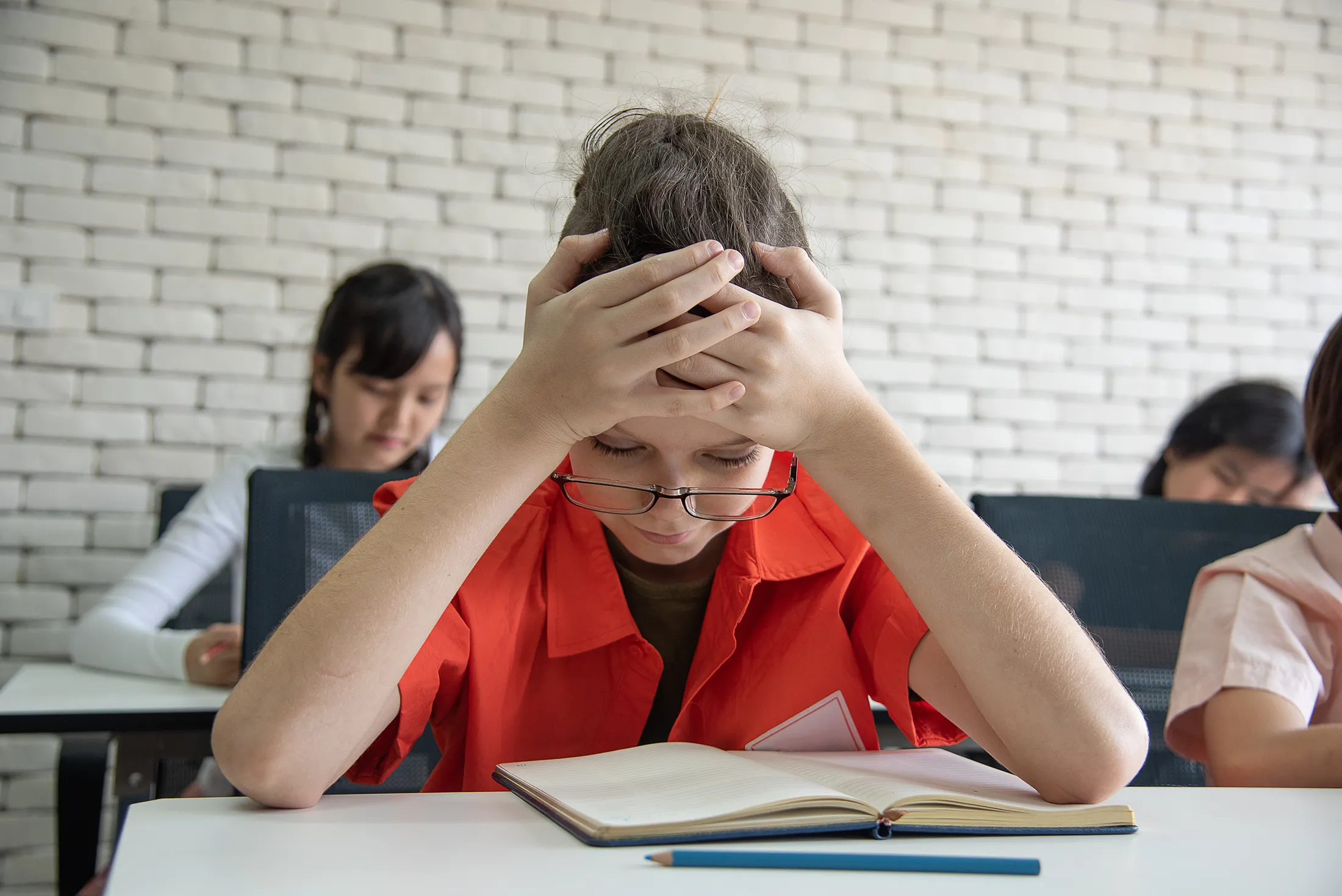 high-school-tudents-feel-bored-and-lazy-to-study-i-2025-01-08-06-12-23-utc Stressed student holding their head while trying to read a book in a classroom.
