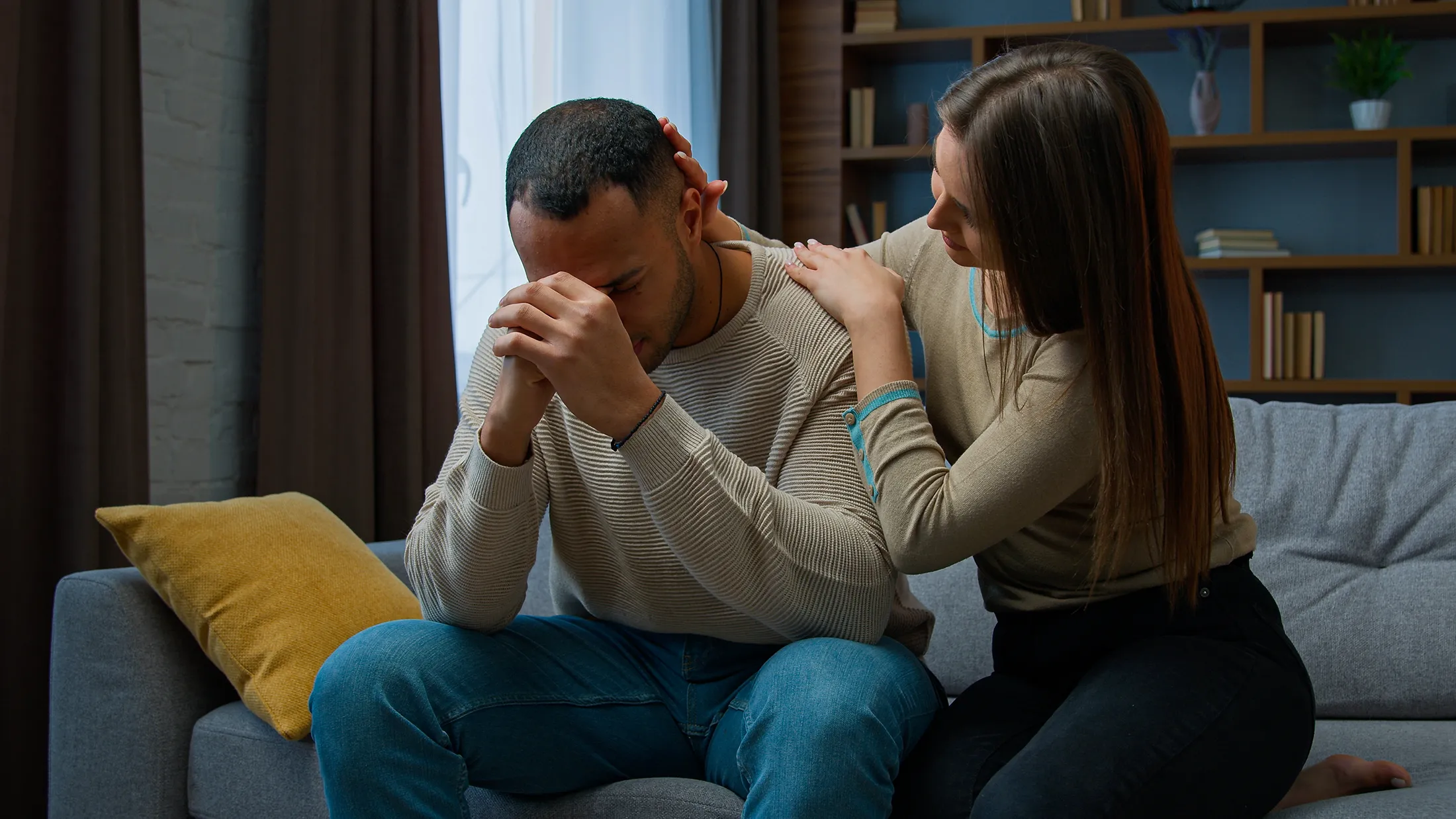 offended-african-american-man-sit-on-couch-upset-w-2025-03-24-00-55-13-utc One partner comforting the other by placing a hand on their shoulder while they sit on a couch, illustrating emotional support during relationship stress or anxiety.